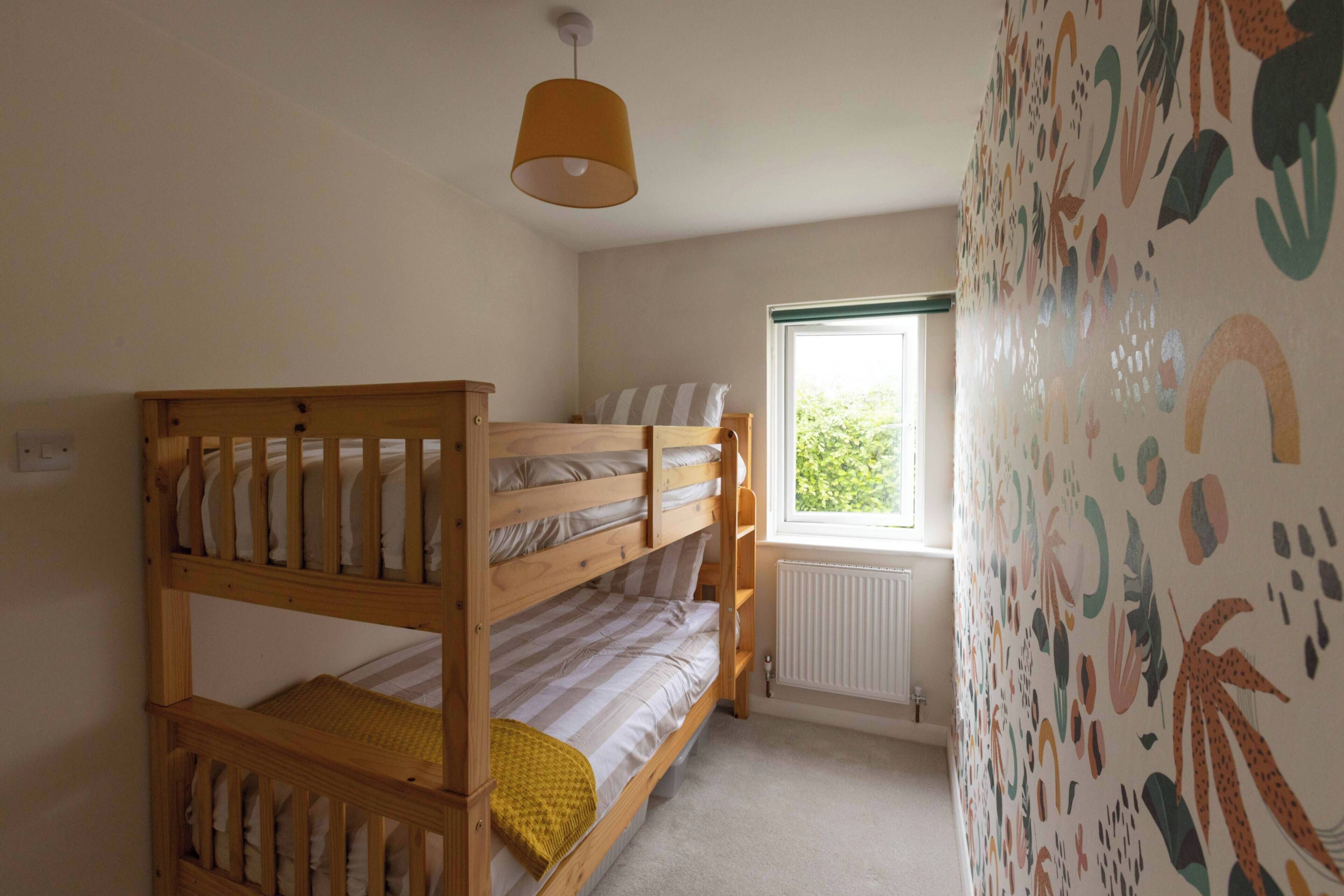A room with a bunk bed, a window with a view, and a wall with a colorful pattern.