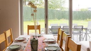 A dining area with a table set for six, chairs, a vase with dried flowers, and a view through a sliding glass door. - House - Sleeps 12 - Parking - Garden (Blandford Forum)