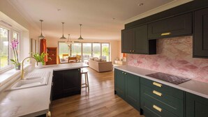 A modern kitchen with a central island, dark cabinetry, and pendant lighting. - House - Sleeps 12 - Parking - Garden (Blandford Forum)