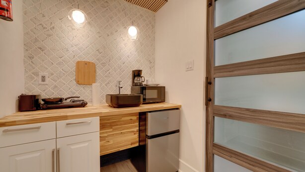 Una cocina compacta con encimera de madera, microondas integrado, refrigerador de acero inoxidable y tabla de cortar de madera en la pared.