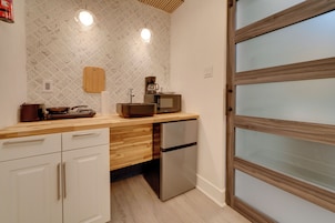 A compact kitchen with a wooden countertop, a built-in microwave, a stainless steel refrigerator, and a wooden cutting board on the wall.