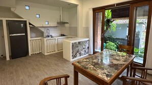 A modern kitchen with a central island, wooden chairs, and a view of greenery outside. - Room-a Quiet Room With Balcony in the he (Ubud)