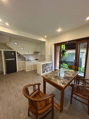 A modern kitchen with a central island, wooden chairs, and a view of greenery outside. - Room-a Quiet Room With Balcony in the he (Ubud)