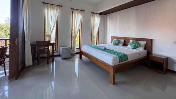 A bedroom with a bed, a chair, a nightstand, and a window with curtains. - Room-a Quiet Room With Balcony in the he (Ubud)