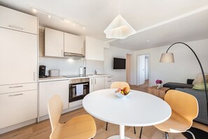 A modern kitchen with white cabinets, a round dining table, and a fruit bowl. - Reichenau Apartment in Salem (Salem)