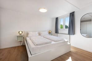 A modern bedroom with a white bed, bedside lamps, a window with curtains, and a round mirror on the wall. - Reichenau Apartment in Salem (Salem)