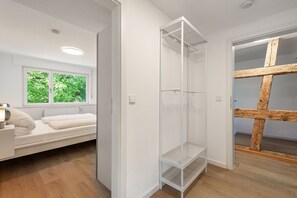 Ein Zimmer mit einer weißen Schrankwand, einem Bett mit weißem Kopfteil und einem Fenster mit Blick auf grüne Vegetation.
