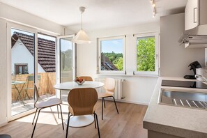 Eine moderne Küche mit Essbereich, großen Fenstern und Blick auf ein Haus.