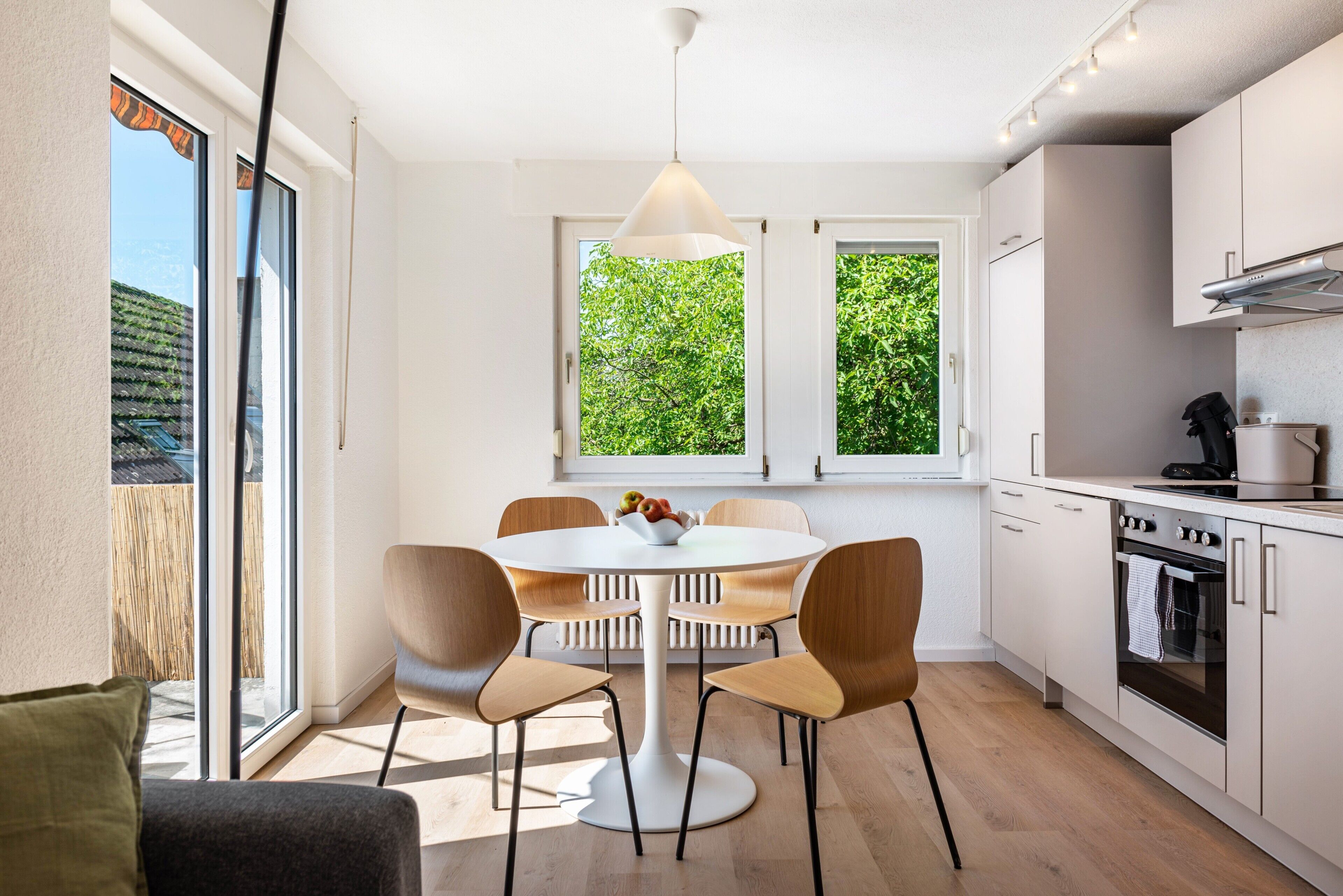 Een moderne keuken met een eettafel, stoelen en uitzicht op groen door de ramen.