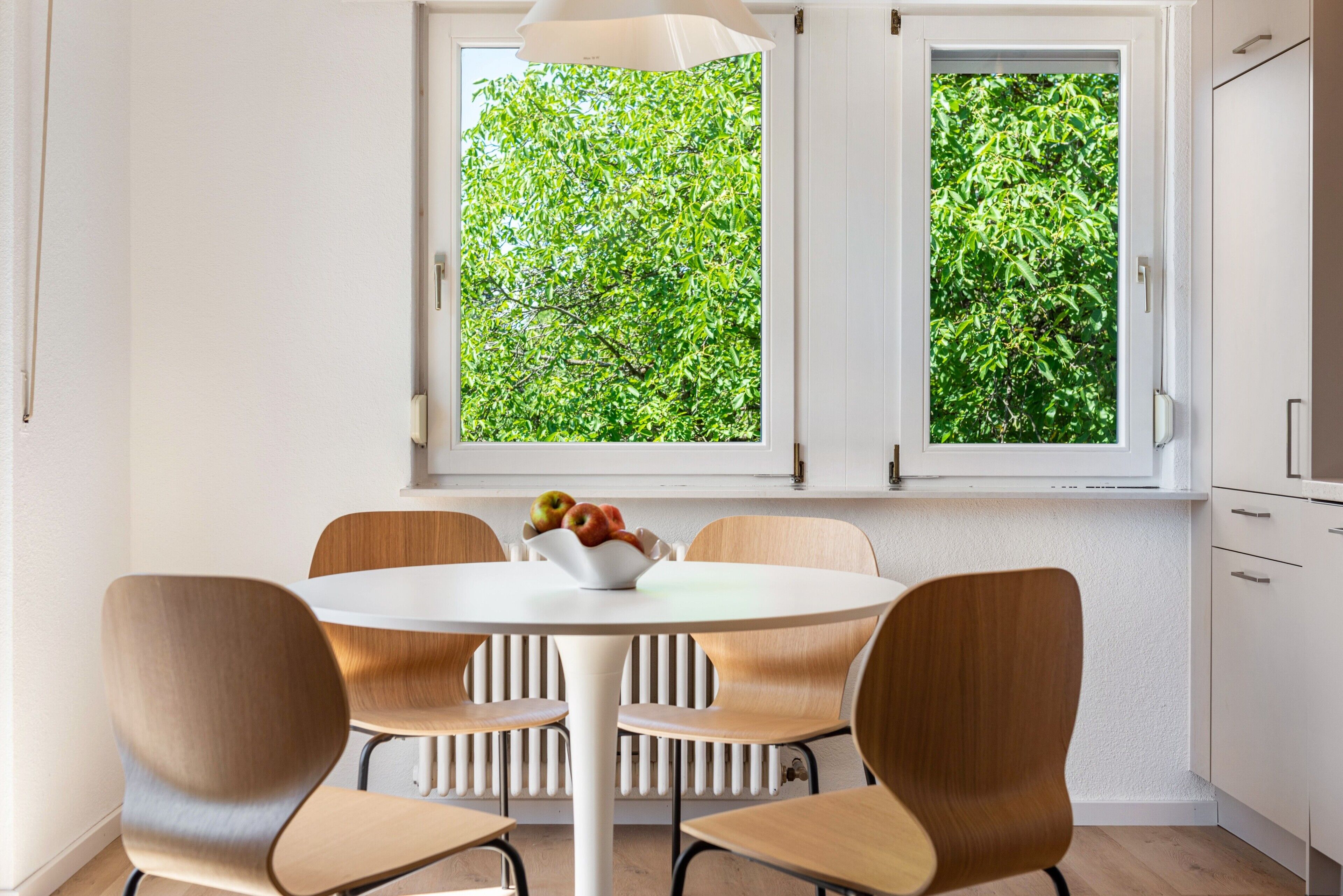 A dining area with a round table, four chairs, and a bowl of fruit.