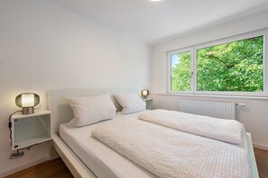 A bedroom with a bed, two bedside lamps, a window with a view of greenery, and a radiator. - Reichenau Apartment in Salem (Salem)