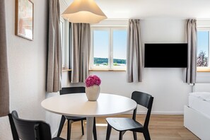 A modern room with a round dining table, two chairs, a vase with flowers, a flat-screen TV, and a bed. - Apartment Mainau with Private Kitchen (Salem)