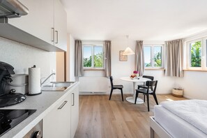 A compact kitchen with a stove, sink, and a roll of paper towels. There is a dining area with a table, chairs, and a window with curtains. - Apartment Mainau with Private Kitchen (Salem)