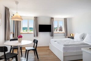 A hotel room with a bed, a desk, a chair, a TV, and a window with curtains. - Apartment Mainau with Private Kitchen (Salem)