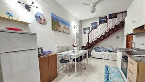 Cocina compacta con refrigerador, una mesa de comedor con sillas, una cafetera y un cuadro en la pared.