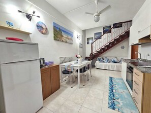 A compact kitchen with a refrigerator, a dining table with chairs, a coffee machine, and a painting on the wall. - Central vacation home that sleeps 6, just 5 meters from crystal-clear beaches (Sardegna)