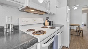 Una cocina con estufa, microondas y horno, un comedor con mesa y sillas, y un ventilador de techo.