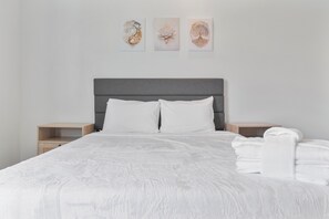 A neatly made bed with white linens, a grey headboard, and a bedside table with a folded white towel.