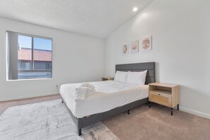 Un dormitorio con cama, mesitas de noche, una ventana y obras de arte en la pared.