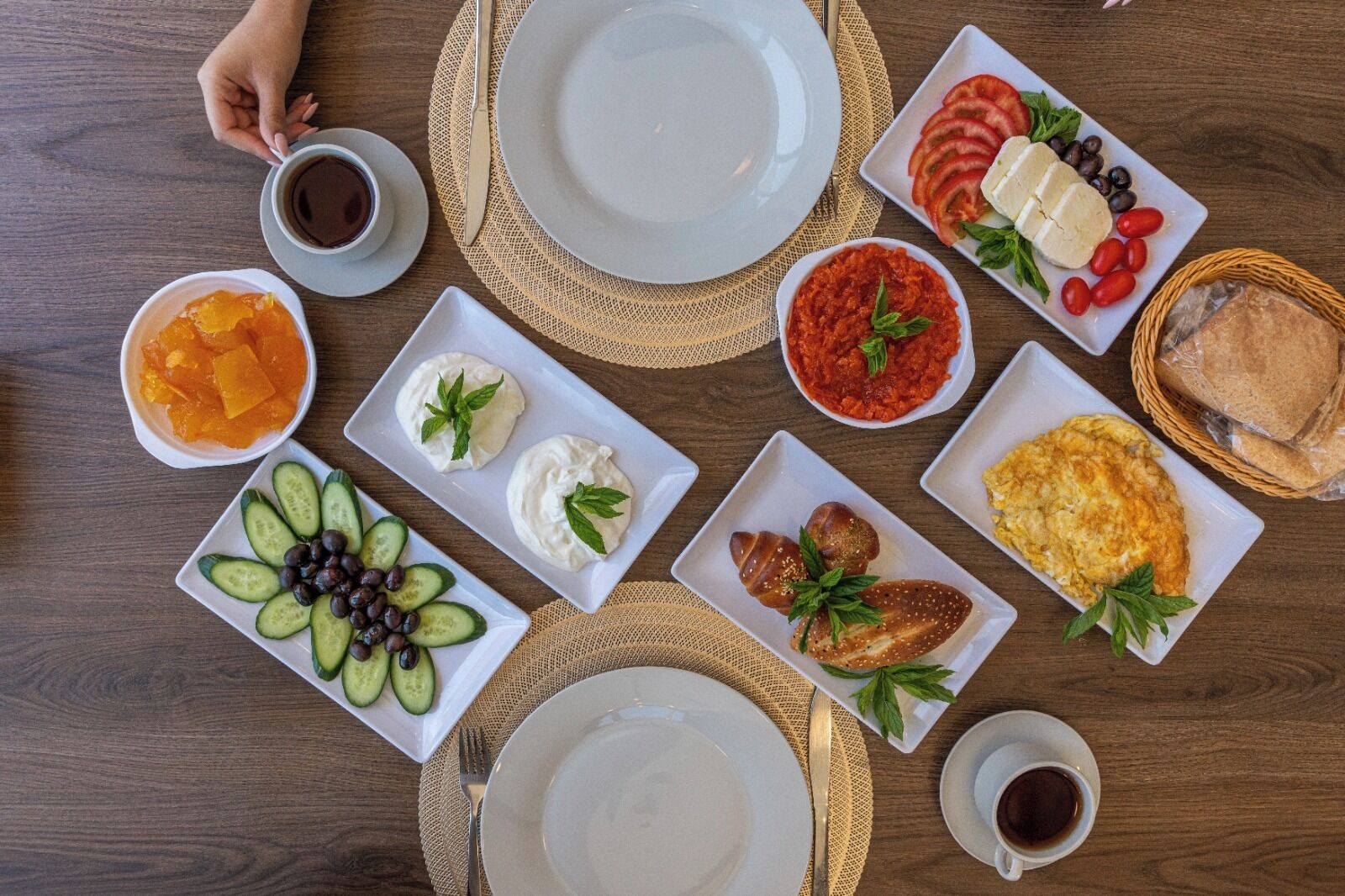 A breakfast setting with plates of food, a cup of coffee, and a basket of bread.