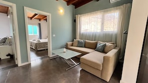 A living room with a sofa, a glass coffee table, and a bed in the background. - Spacious Country House Near Fataga (San Bartolomé de Tirajana)