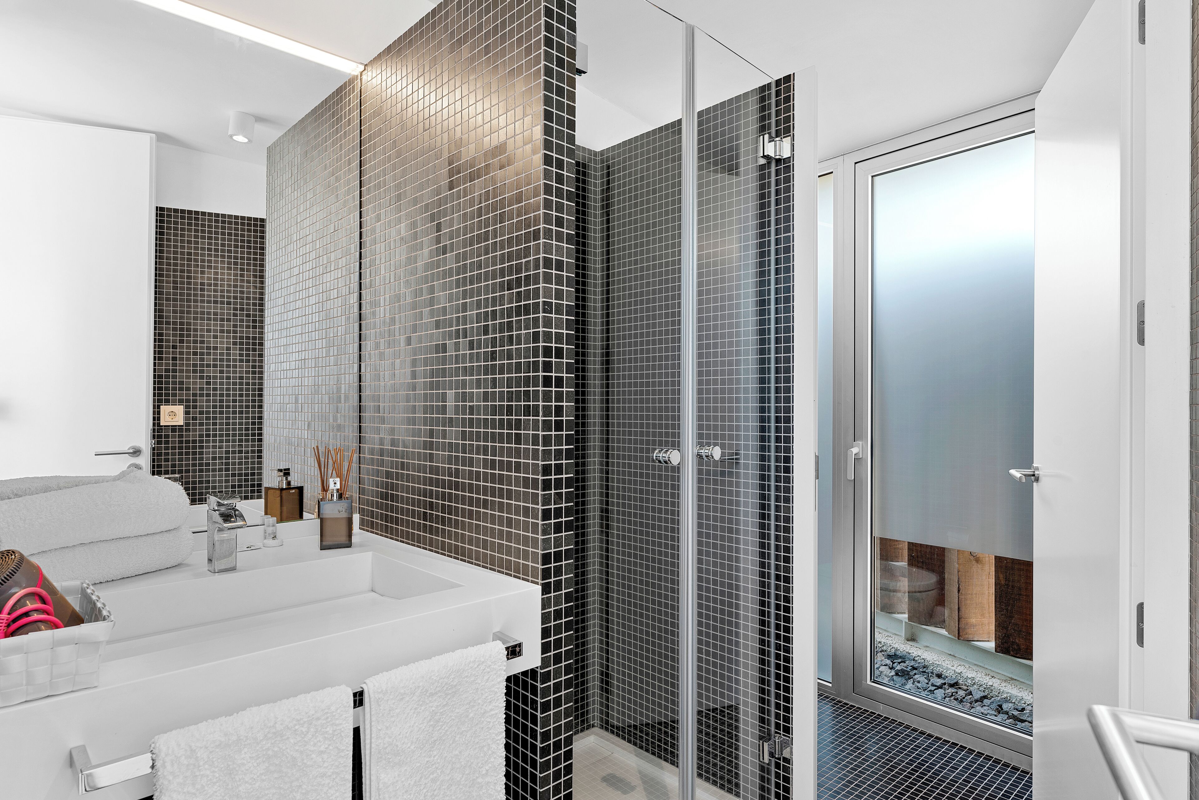 A modern bathroom with a glass shower enclosure, a white sink, and a mirror.