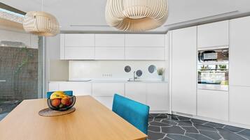 A modern kitchen with white cabinetry, a dining table with a fruit bowl, and a blue chair.