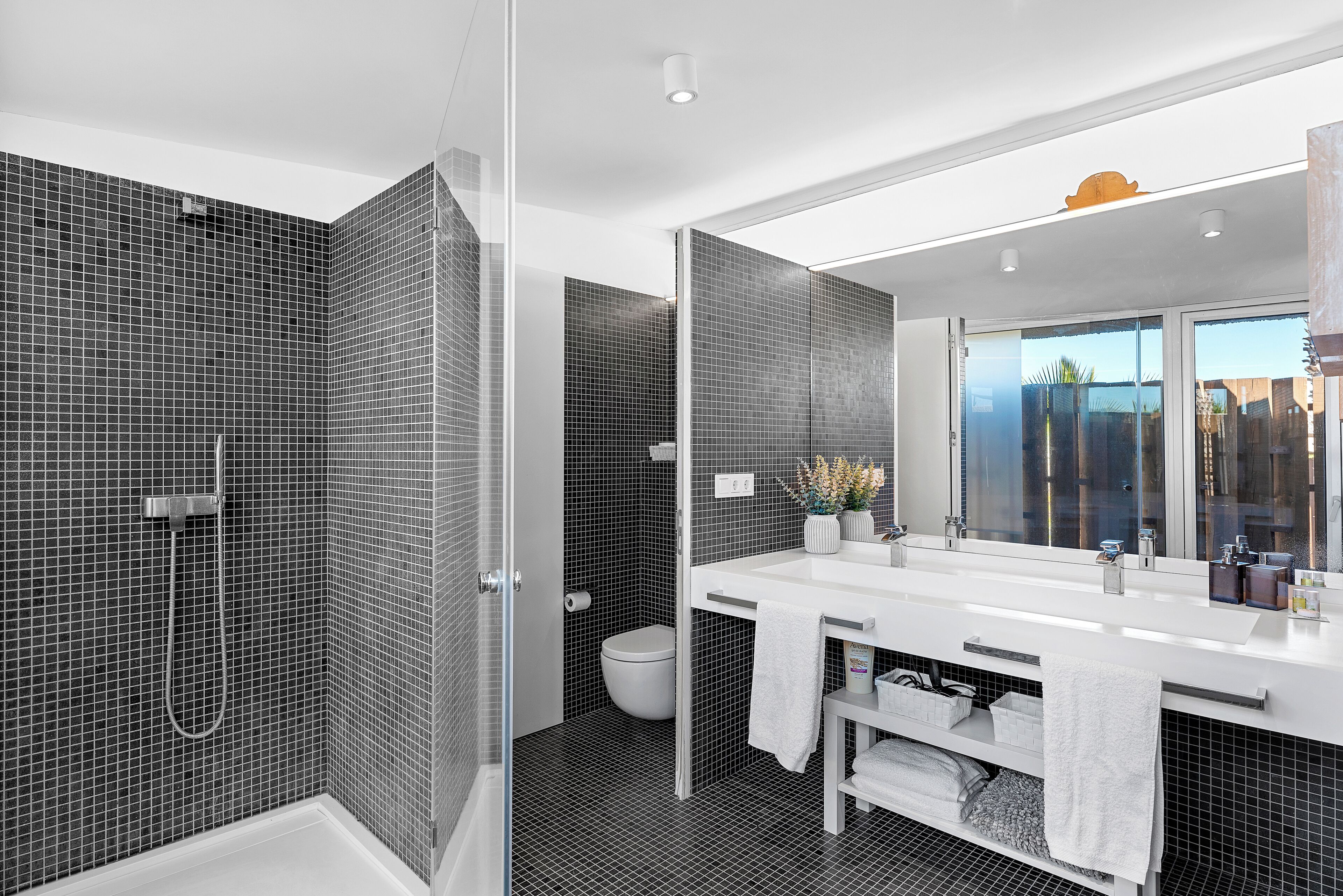 Une salle de bain moderne équipée d’une douche, de toilettes et d’un grand miroir.