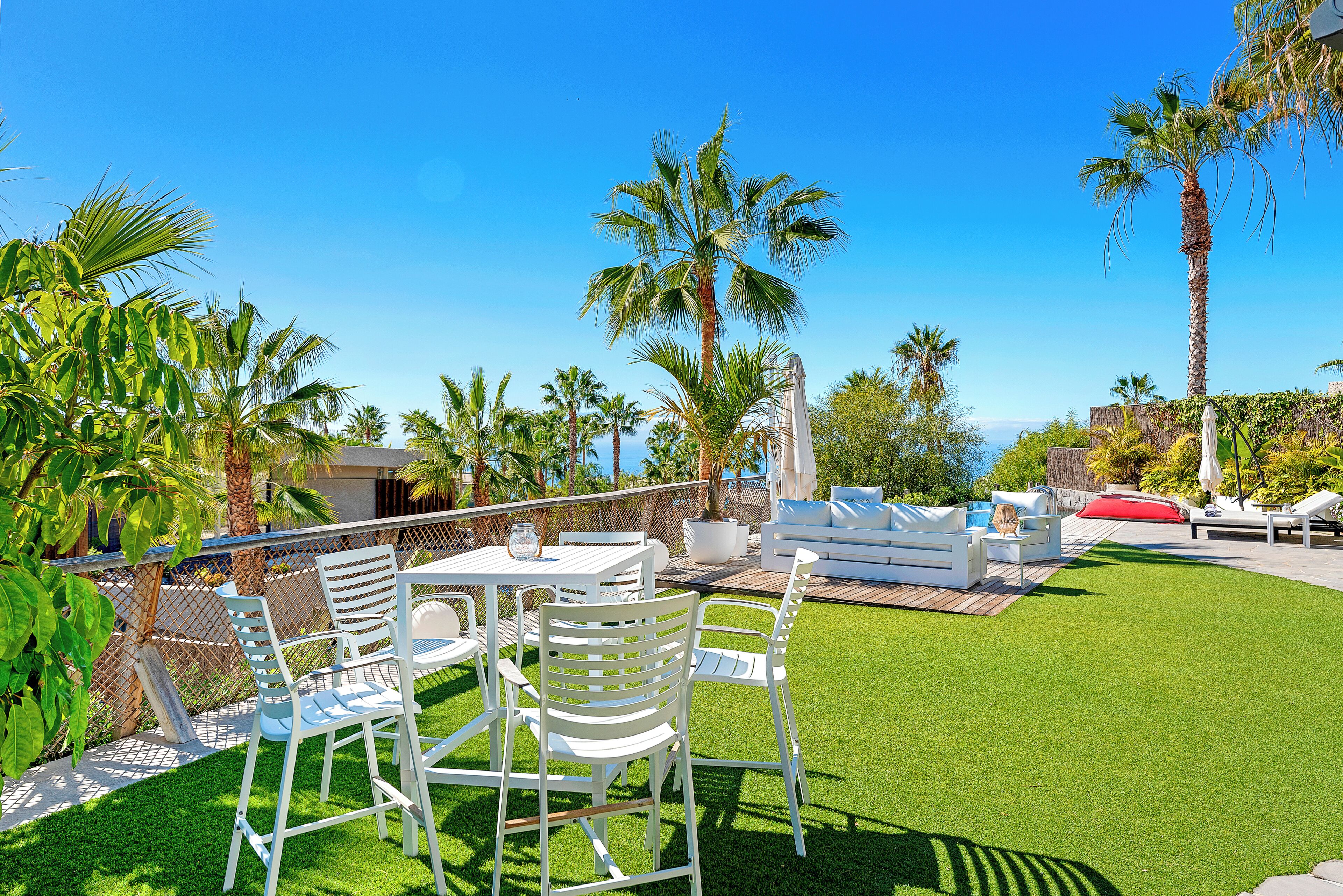 An outdoor patio with white furniture, palm trees, and a clear blue sky.