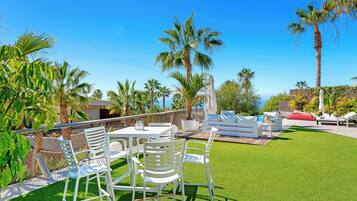 An outdoor patio with white furniture, palm trees, and a clear blue sky.