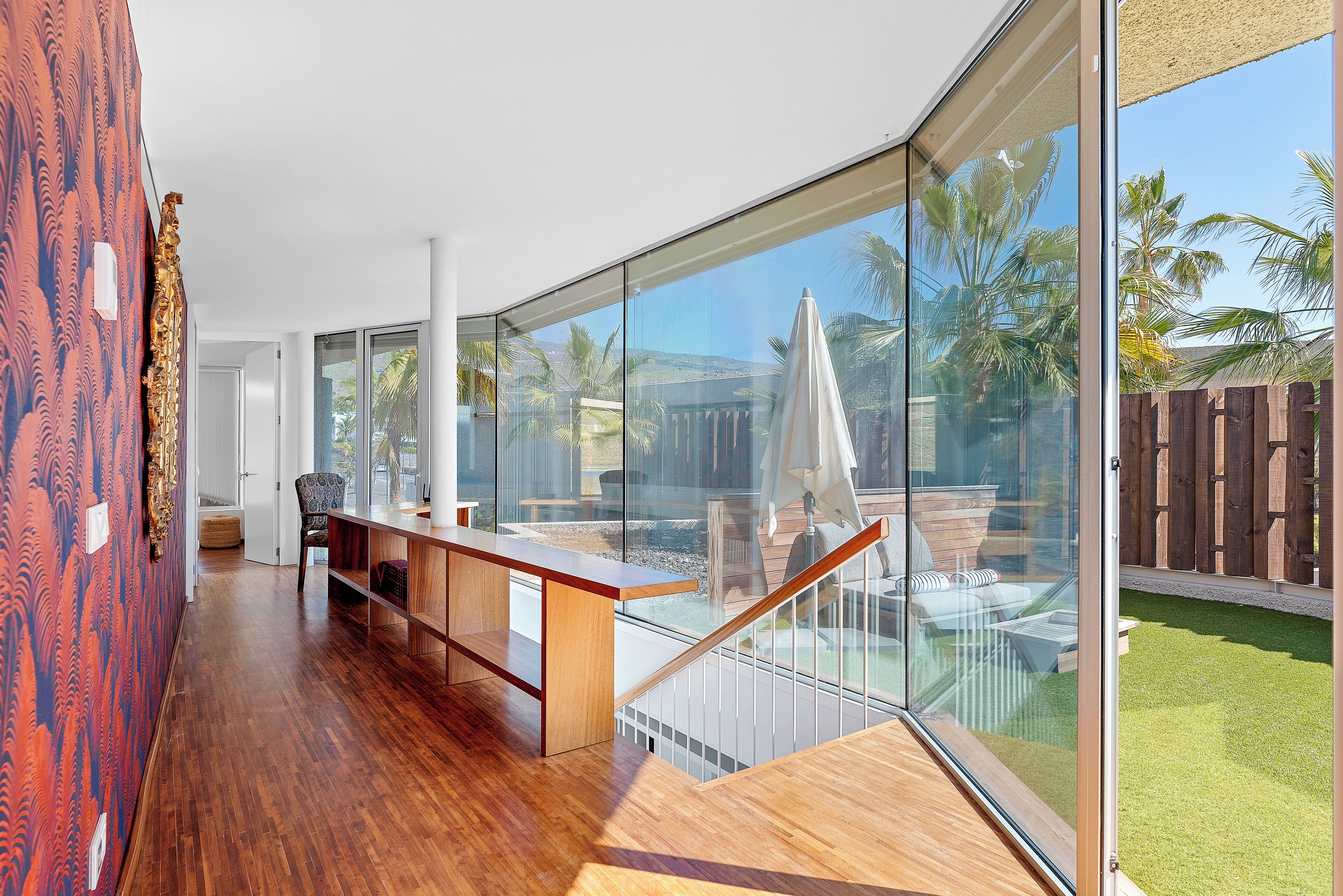 Ein geräumiges Zimmer mit Holzboden, einer Bank und einer Glaswand mit Blick auf Garten und Pool.