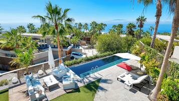 A pool area with lounge chairs and a view of the ocean.