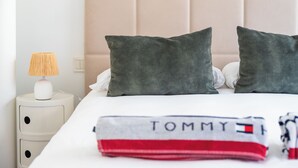 Un lit bien fait, avec deux oreillers, une lampe de chevet et une serviette pliée portant le nom d’une marque.