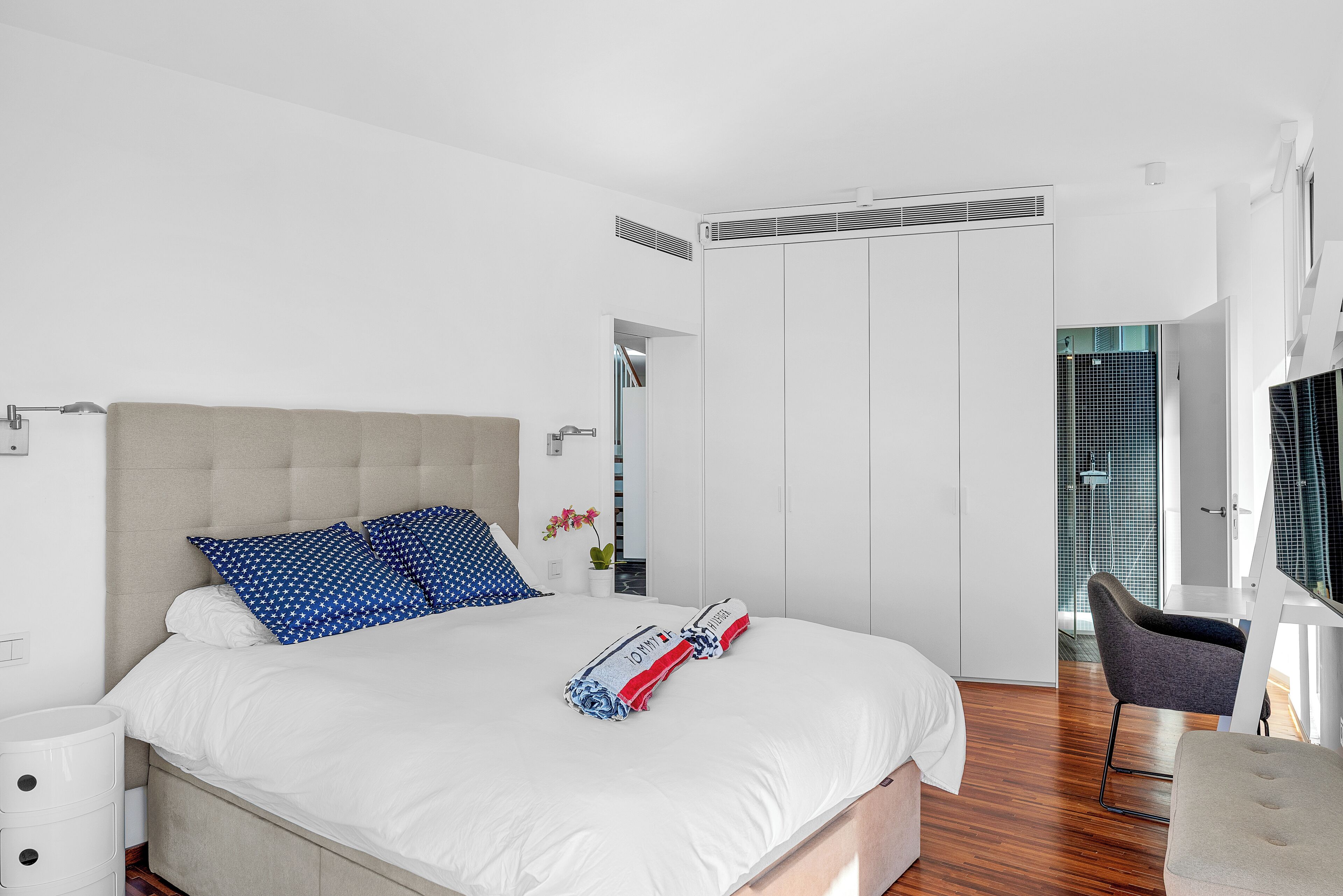 Une chambre moderne avec un grand lit, une table de chevet, une chaise et un dressing.