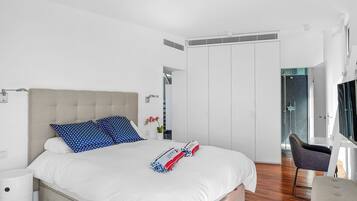 A modern bedroom with a large bed, a bedside table, a chair, and a walk-in closet.