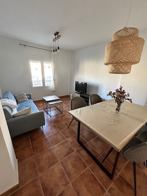 Ein Wohnzimmer mit einer Couch, einem Esstisch, einem Fernseher und einer Pendelleuchte.