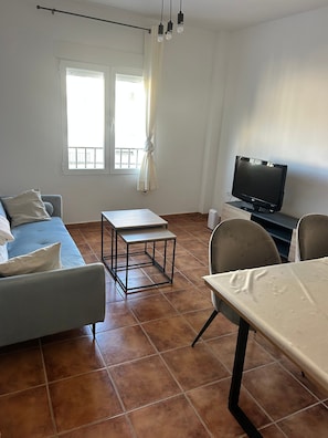 Een woonkamer met een bank, een salontafel, een televisie en een eettafel.