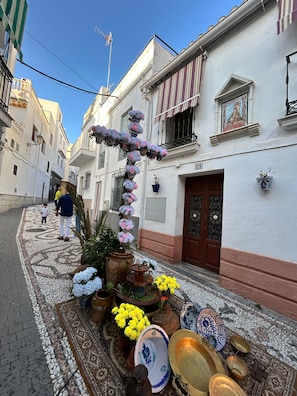 Eine enge Straße mit Häusern, einer Zierdekoration aus Blumen und traditionellem Geschirr.