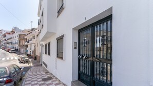 Una calle estrecha con coches aparcados y un edificio con un portón negro grande.