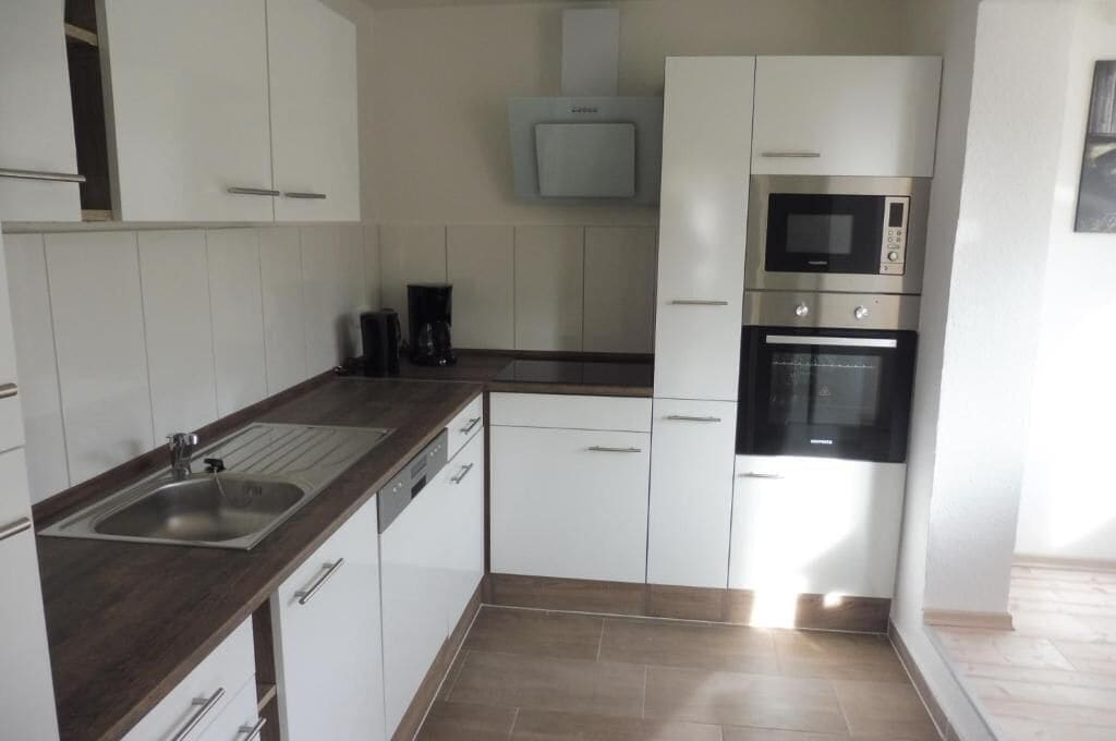 A kitchen with white cabinets, a stainless steel sink, a microwave, and an oven.