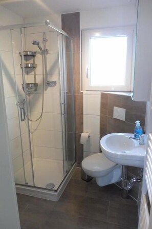 Ein Badezimmer mit Duschkabine aus Glas, einem weißen Waschbecken und einer Toilette.