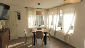 Uma sala de jantar com uma mesa e cadeiras, um lustre pendurado e vista para o exterior através de grandes janelas.