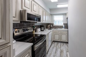A modern kitchen with white cabinets, a black stove, and a microwave. - CNB10- West Beach Jewel! Amazing View! Enjoy The Beach & Lagoon! (Gulf Shores)