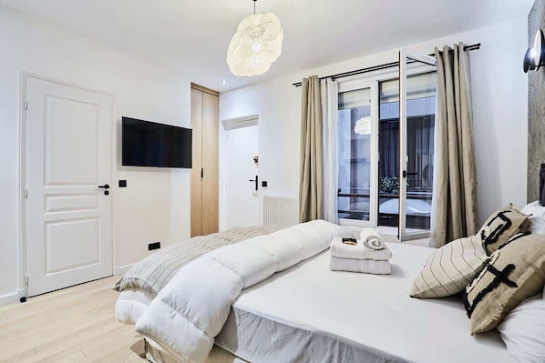 A bedroom with a bed, a television, a window with curtains, and a door. - Superb Studio in the Center of Paris/Opera (Paris)