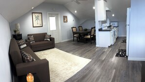 A living room with a brown sofa, a dining table with chairs, a kitchen area with a microwave, and a ceiling fan. - Charming 3-bedroom house in adorable Bodden Town with AC (Bodden Town)