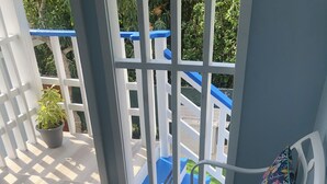 A balcony with white metal railings, a potted plant, and a blue mat. - Charming 3-bedroom house in adorable Bodden Town with AC (Bodden Town)