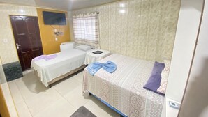 A room with two beds, a toilet, a TV, and a window with curtains.