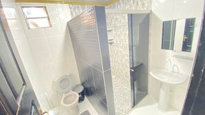 A bathroom with a shower, two toilets, a sink, and a mirror.