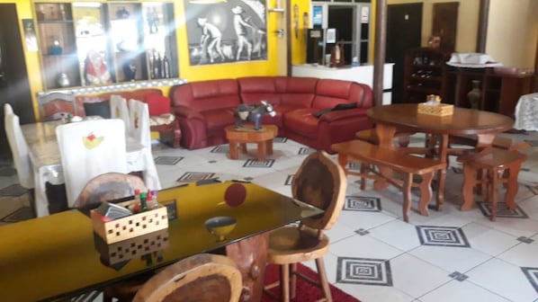 A living room with a red sofa, wooden chairs, a yellow table, and a tiled floor. - HOTEL E RESTAURANTE MAMÃE QUERO MAIS (Magalhães Barata)