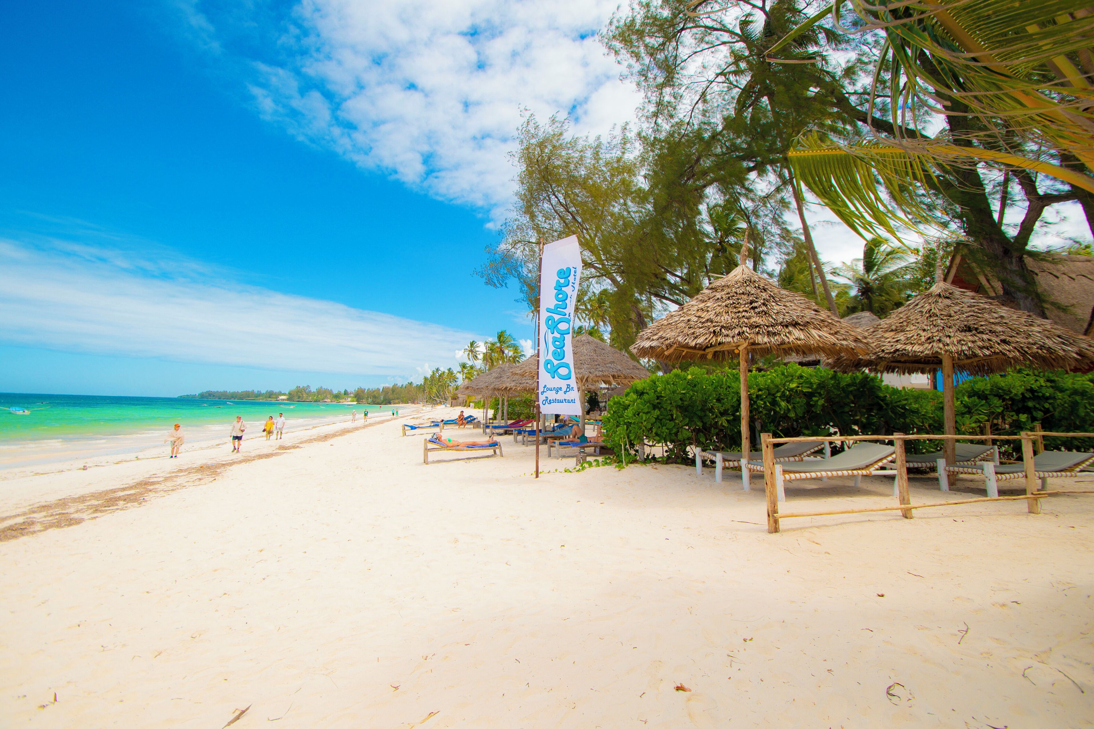 A beach with thatched umbrellas, a lounge bar, and a restaurant sign.